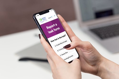 A woman's hand using a mobile phone to report a leak on United Utilities' website